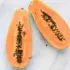 Two halves of a ripe papaya with seeds on a marble surface.