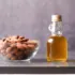 Glass bowl of almonds next to a small bottle of almond oil on a grey surface.