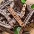 Carob pods and seeds on a wooden surface with green leaves.