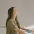 Woman sitting with eyes closed in sunlight, wearing a khaki shirt.