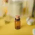 Small amber glass bottle with cork on yellow surface, surrounded by stones and flowers.