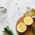 Lemon halves, ginger, mint, supplements, and a strainer on a marble surface.