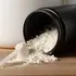 Black container of white powder with scoop on wooden surface.