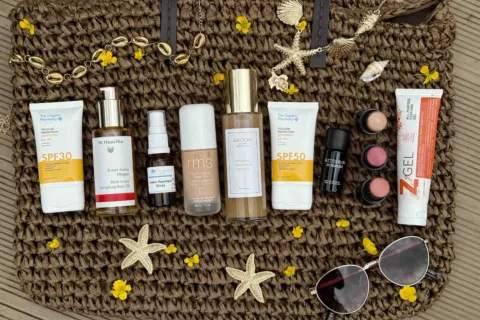 Skincare products on a woven bag with starfish, shells, and sunglasses.