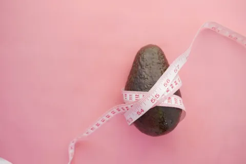 Avocado wrapped with a measuring tape on a pink background.