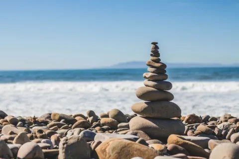 Stack of balanced stones on a pebble beach with ocean waves in the background.