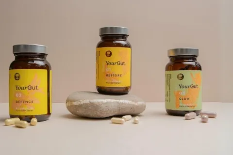 Three jars of YourGut supplements with capsules on a beige surface.