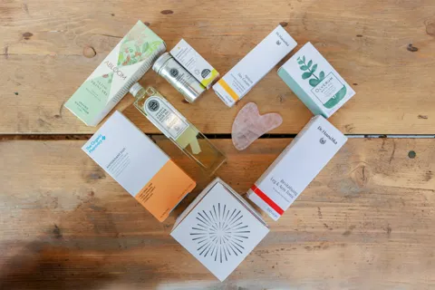 Skincare products and a pink gua sha stone arranged on a wooden surface.