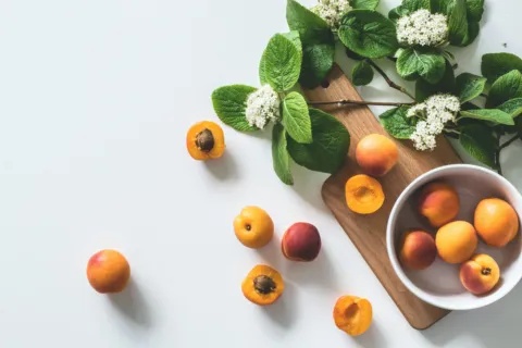 Apricots and green leaves on a wooden board with white flowers.
