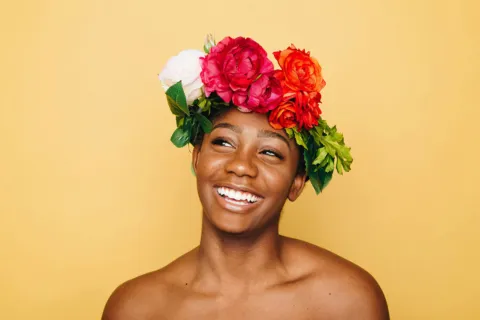 Smiling person wearing a colourful flower crown against a yellow background.