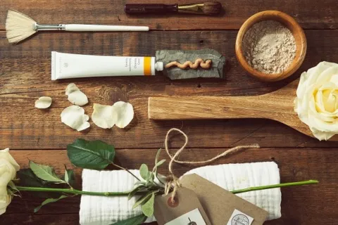 Skincare items, white roses, and petals on a wooden surface.