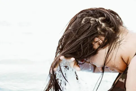 Wet hair being rinsed in water, person leaning forward.
