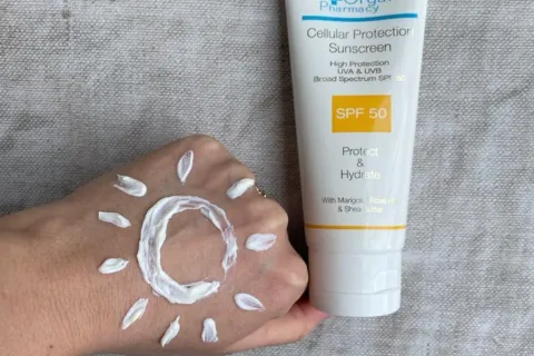 Hand with sunscreen in sun shape, next to SPF 50 sunscreen tube on fabric background.