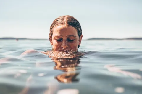 Person with wet hair emerging from water in a calm lake.