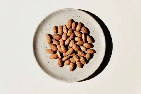 Almonds on a speckled ceramic plate against a light background.