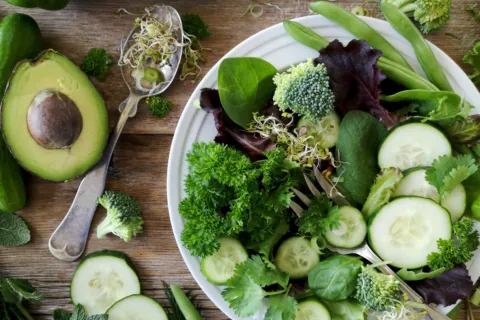 Salad with cucumber, avocado, sprouts, and greens on a wooden table with fresh vegetables.