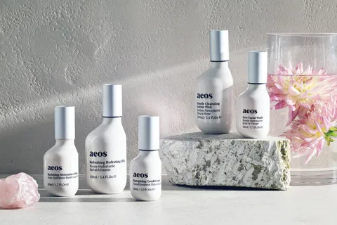 Aeos skincare bottles on stone with pink flowers in water.