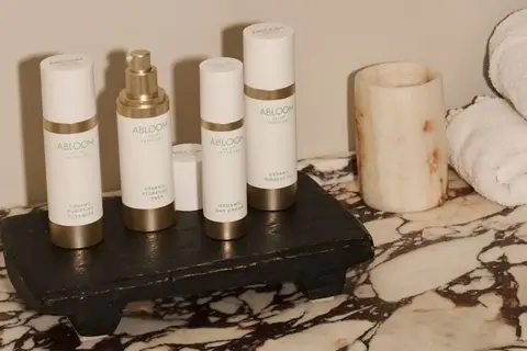 Skincare products labelled "ABLOOM" on a marble surface with rolled towels.