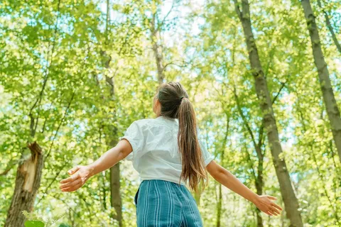 Woman with arms outstretched in a sunlit forest.
