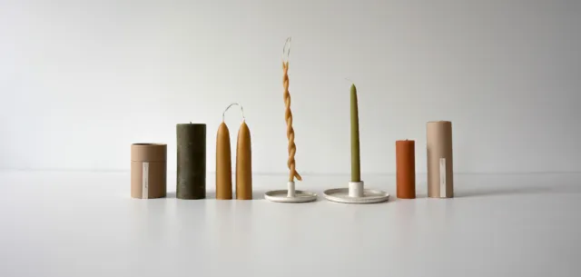 Assorted candles and holders on a white surface, with cardboard packaging.