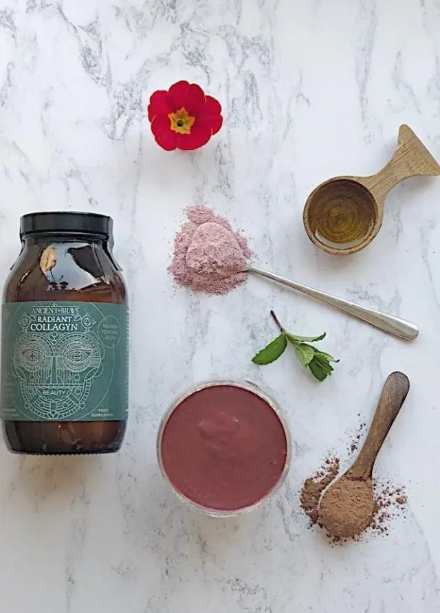 Collagyn jar, red flower, powders, mint, and wooden spoon on marble surface.
