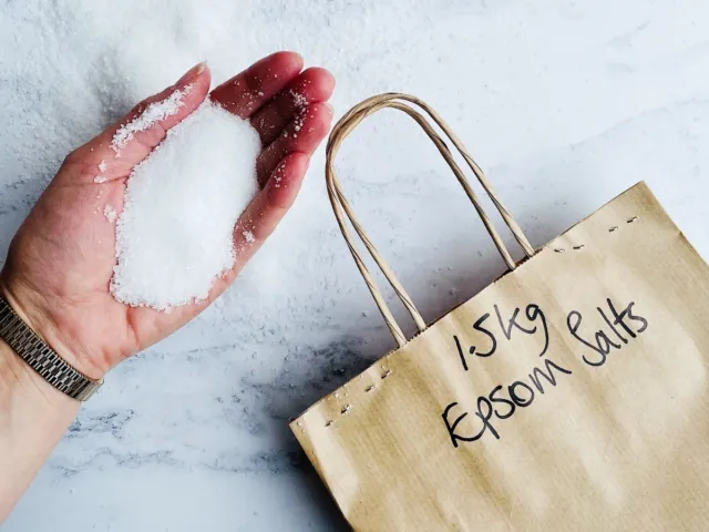 Hand holding Epsom salts next to a paper bag labelled "1.5kg Epsom Salts".