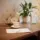 Teapot, teacup, and paper on wooden table with plant and water jug in background.