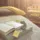 Open book, eucalyptus leaves, and candles on a spa bed with a yellow towel in a softly lit room.