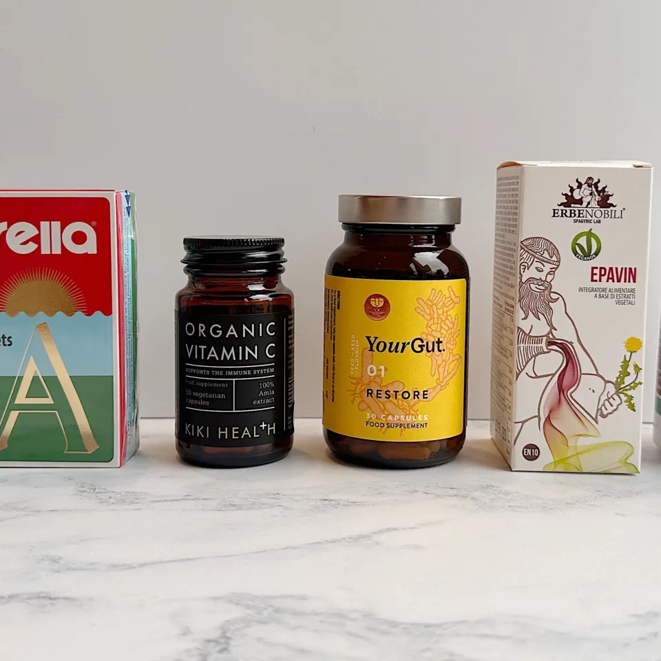 Five supplement bottles and boxes on a marble surface, including chlorella and vitamin C.