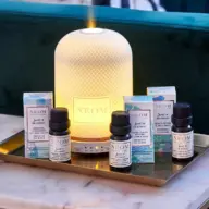 NEOM diffuser with essential oils on a tray, set against a green sofa.