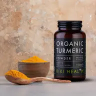 Kiki Health Organic Turmeric Powder jar, wooden bowl, and spoon on a stone surface.