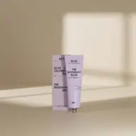 AKT deodorant balm tube and box on a beige surface with soft shadows.