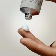 Hand cream being applied to a fingertip from a tube.