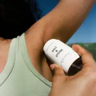 Person applying Salt & Stone deodorant to armpit outdoors.