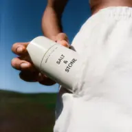 Person holding Salt & Stone deodorant against white trousers outdoors.