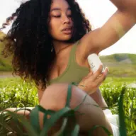 Person applying deodorant outdoors in a grassy field.