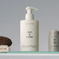 Salt & Stone body lotion and deodorant on a glass shelf with a pumice stone and towel.