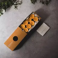 Box of eight yellow candles on grey surface with green ivy.