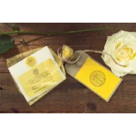 Skincare product with yellow label, gift tag, and white rose on wooden surface.