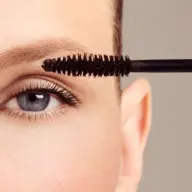 Close-up of a mascara wand near an eye with long lashes.