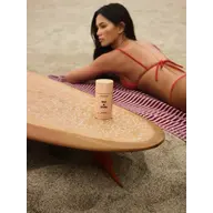 Deodorant stick on surfboard, woman in red bikini on sand.