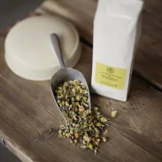 Herbal tea blend with scoop and white packet on wooden table.
