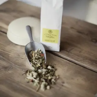 Herbal tea blend in a scoop on wooden table, with a white bag labelled "Immuni-Tea".