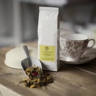 Herbal tea blend labelled "Digestivi-T" with a scoop and floral teacup on a wooden table.