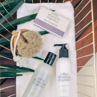 Skincare products and brush on a towel with green leaves.