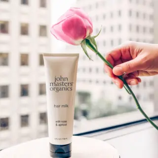 Tube of John Masters Organics hair milk with a pink rose held nearby.