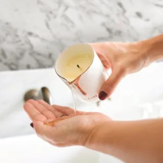 Hands pouring melted candle wax into palm over a marble sink.