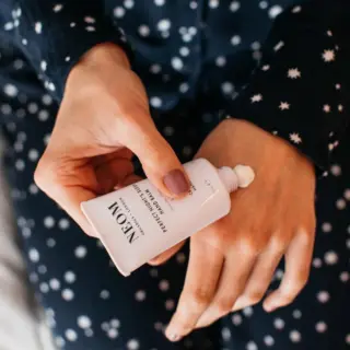 Hands applying NEOM hand balm in a star-patterned outfit.