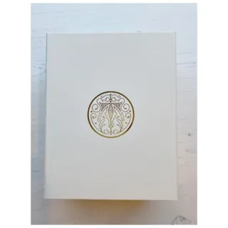 White box with ornate gold circular emblem on a light wooden surface.