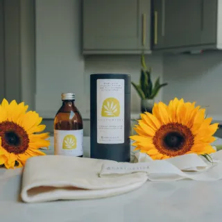 Castor oil bottle, cylindrical box, cloth, and two sunflowers on a kitchen counter.